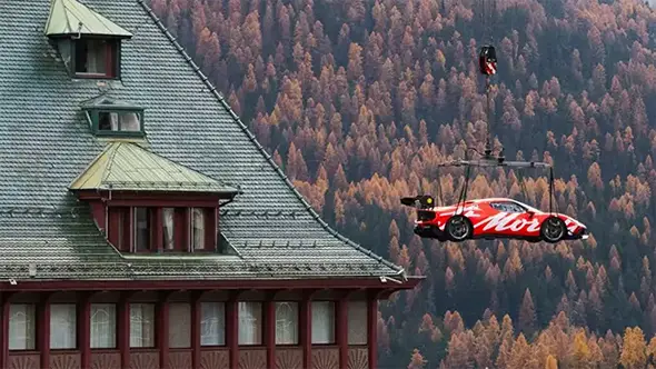 A Ferrari sports car being lifted by a crane against an autumn forest background near Badrutt’s Palace hotel.
