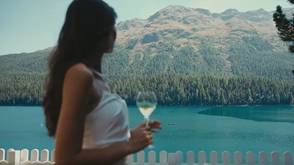 A lady with a glass of wine on the Badrutt’s Palace terrace enjoying the view of Lake St. Moritz and the Alps.