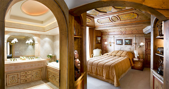Luxury bedroom with bathroom in La Loze apartment, Courchevel 1850: golden bedspread, painted wooden ceiling, arched door to marble bathroom with lighting.