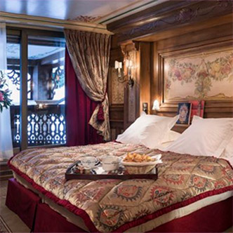 Luxury bedroom in Le Sommet apartment, Courchevel 1850: large bed with burgundy bedspread, breakfast tray, fresco above headboard and balcony with mountain view.