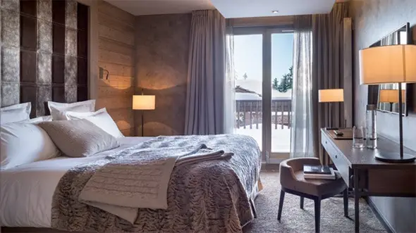 Luxury bedroom in Grandes Alpes Hotel Courchevel 1850: cozy interior with panoramic snowy slopes and balcony view