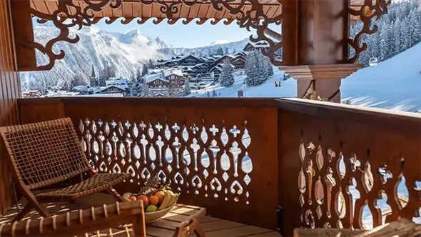 View from a carved wooden balcony of Hotel de La Loze overlooking the snow-covered mountains and Alpine village.