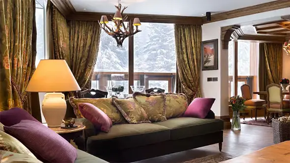 Elegant living room in Hotel de La Loze suite featuring classic Alpine decor and winter forest views.