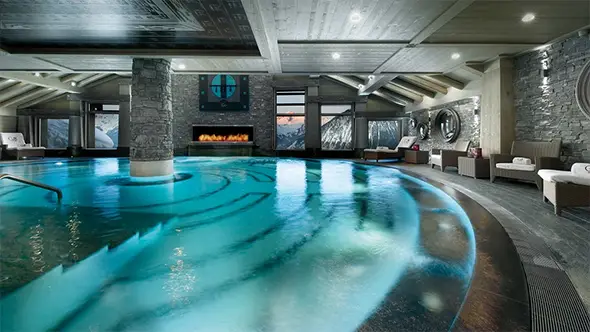 Luxurious indoor swimming pool at a Méribel hotel spa with fireplace, panoramic mountain views and lounge area.