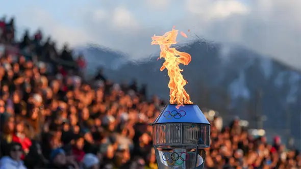 The Olympic flame against a backdrop of mountains, symbolizing the start of the Milano-Cortina 2026 Games.