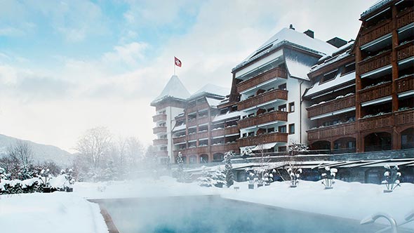 Winter facade of The Alpina Gstaad with heated outdoor pool against snowy mountains