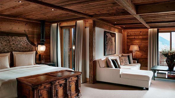 Luxury suite at The Alpina Gstaad: bedroom with wooden walls and cozy living area with mountain views