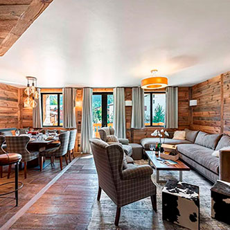 Elegant living-dining room in Le Petit Alaska apartment, Val d&rsquo;Is&egrave;re: gray sofa, checkered armchairs, set round table and wooden walls.
