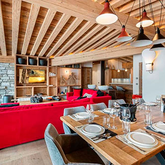 Spacious open living-dining room in Chamois penthouse, Val d&rsquo;Is&egrave;re: bright red sofa, set wooden table and modern lamps.