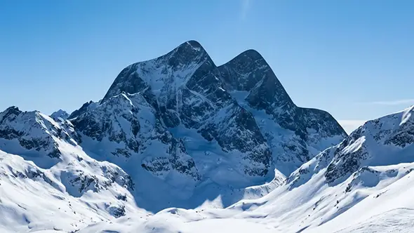 View of snow covered Alpine ridges under a bright blue sky during the spring period.