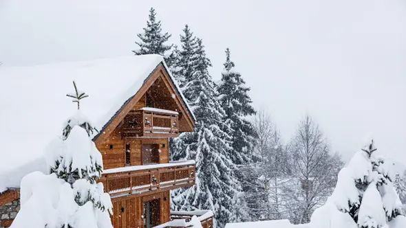 Exterior of Le Coucou 5* hotel in Meribel, covered in snow and surrounded by pine trees