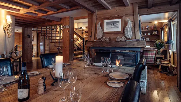 Cozy dining area of a premium Meribel chalet with a set table by the fireplace in the evening