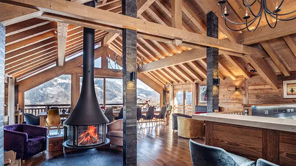 Spacious open-plan living room in a premium Meribel chalet featuring a designer fireplace, panoramic windows, and light wood finishes