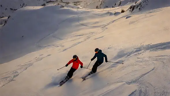 A couple of skiers descending through fresh powder on the sunny slopes of Meribel