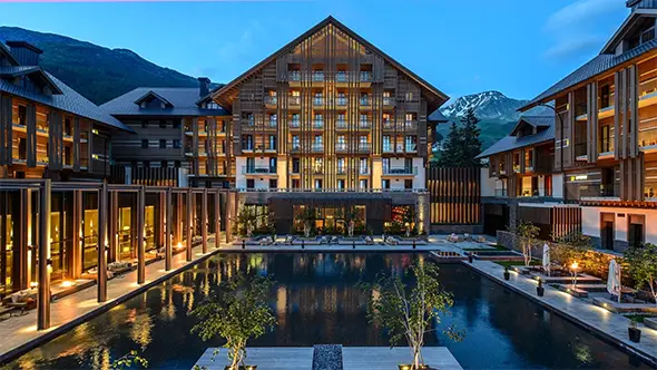 The Chedi Andermatt hotel exterior at dusk with snow-capped Alpine mountains.