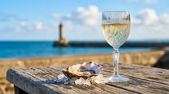 A fresh oyster on ice and a glass of white wine with a sea and lighthouse view.