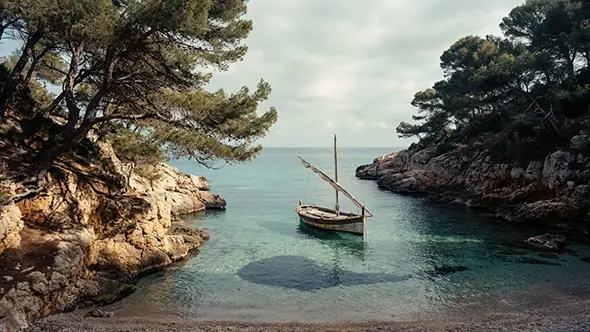 A small boat in a quiet rocky cove with clear water.
