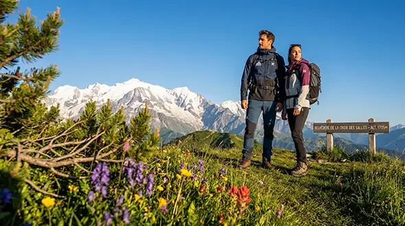 A couple of tourists against the mountains by the Belvedere de la Croix des Salles sign.