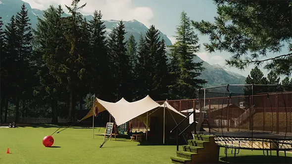 Kids play area with a tent and trampoline near mountains.