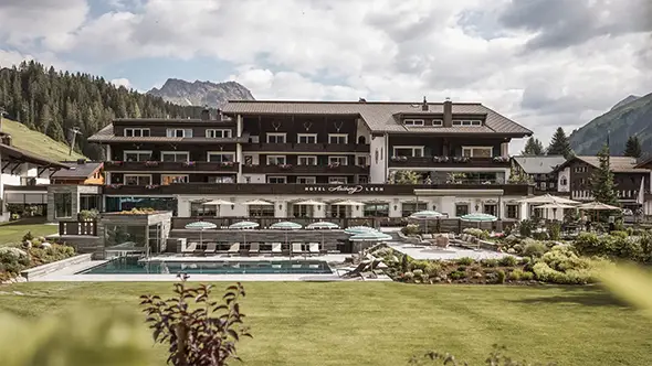 Exterior of Hotel Arlberg Lech with pool in summer.