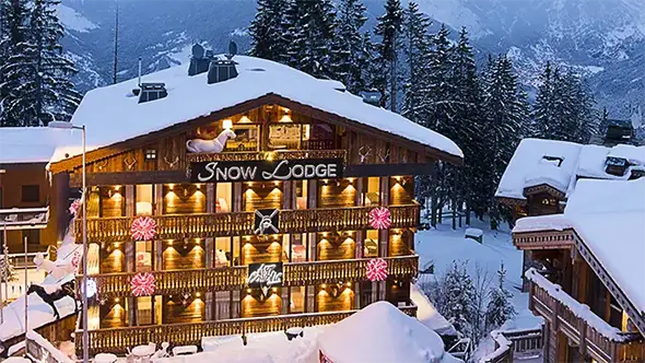 Exterior view of Snow Lodge hotel in Courchevel on a snowy evening.