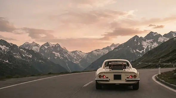 Retro sports car with a suitcase driving on an alpine pass at sunset.