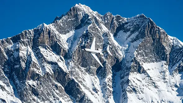 White private jet flying over snowy mountain peaks.
