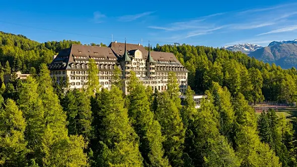 Exterior view of the Suvretta House hotel in St. Moritz, surrounded by forest.