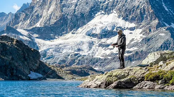 A fisherman fly fishing at a high altitude mountain lake with a glacier in the background.
