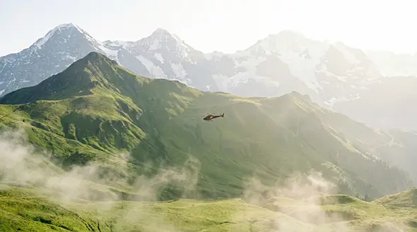 A helicopter performing a transfer over green mountain slopes in the Zermatt area.