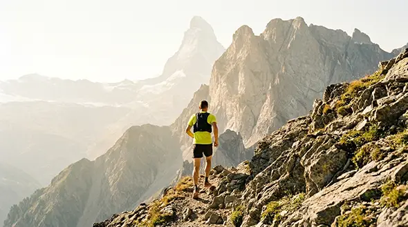 An athlete trail running on a mountain path with a view of the Matterhorn.