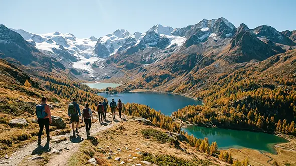 Hikers on a mountain trail above Engadin valley lakes in autumn.