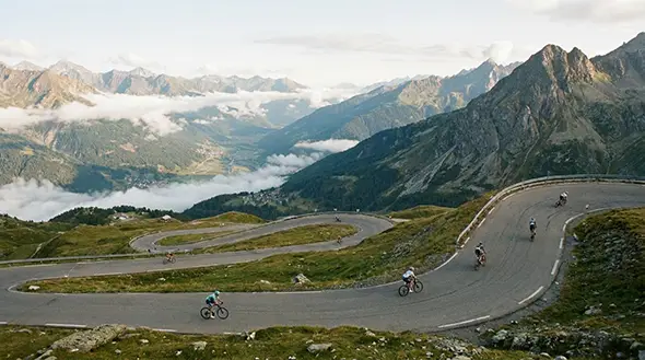 Cyclists riding on a winding mountain road in the Alps.