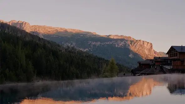 First light on the Dolomite wall above Aman Rosa Alpina, mist rising off still water