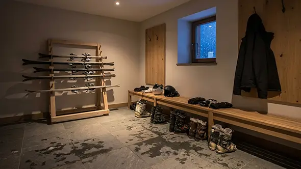 Chalet ski room at the end of the day with boots lined up to dry, skis racked and a jacket on a hook