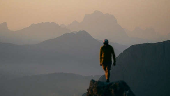 Hiker silhouetted on a rock outcrop above layered Dolomite ridges at sunrise