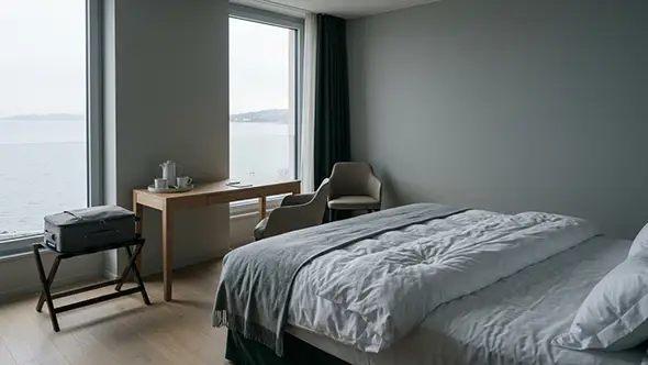 Calm hotel room with a desk and a full-height window onto a grey lake in winter