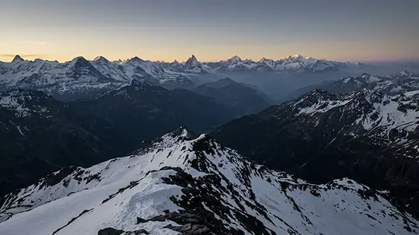 Aerial view over the snow-covered Swiss Alps at dusk with ridge after ridge to the horizon