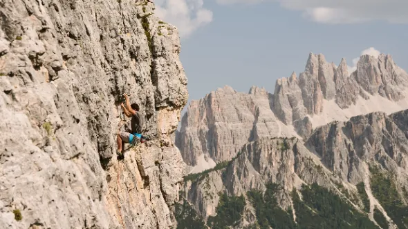 Climber on a via ferrata rock face with Dolomite spires beyond in Alta Badia