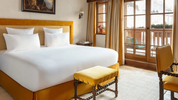 Bedroom with a mustard velvet headboard and a balcony door facing the slopes at Airelles Val d’Isere