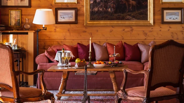 Pine-panelled living room with a red sofa and oil paintings in Chalet Schuss, Val d’Isere