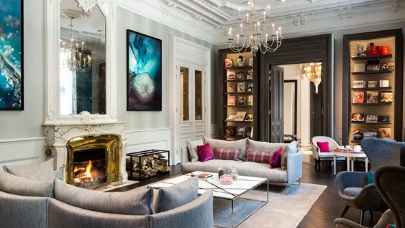 Lounge with a marble fireplace, grey sofas and bookshelves at Hôtel Mont-Blanc Chamonix