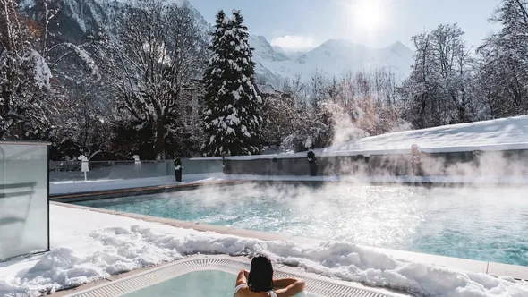 Steaming outdoor pool and whirlpool among snowy fir trees at Hôtel Mont-Blanc Chamonix