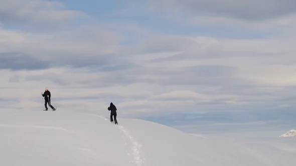 Two ski tourers climbing a wide empty snow slope above Courchevel under a pale sky