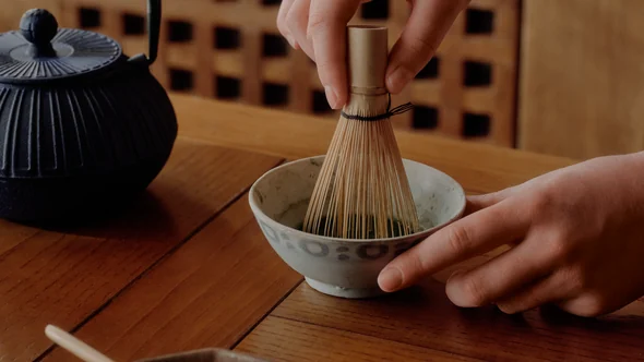 Matcha being whisked beside a cast-iron teapot on an oak table at Aman Le Melezin