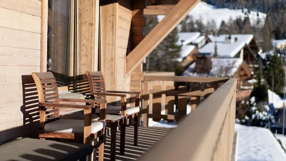 Sunlit chalet balcony with wooden armchairs above the snow-covered roofs of Verbier