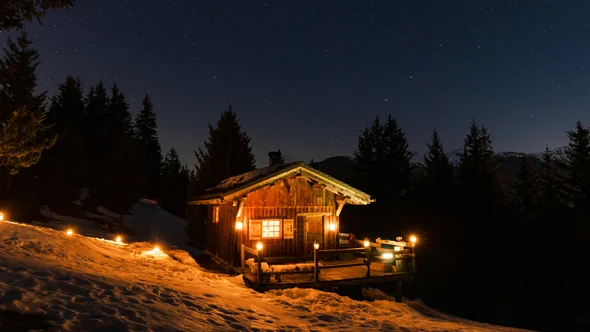 Lit mountain chalet at Les Pres de la Croix on a snowy slope under a starry sky near Courchevel