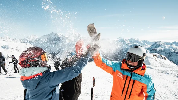 Three skiers throwing snow in the air on a sunny piste in Val Thorens
