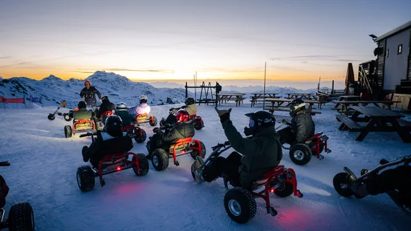 Riders in helmets on three-wheeled mountain karts on a groomed piste in Val Thorens at dusk