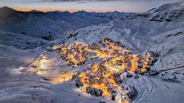 Val Thorens village lit up at dusk under snowy slopes, seen from above